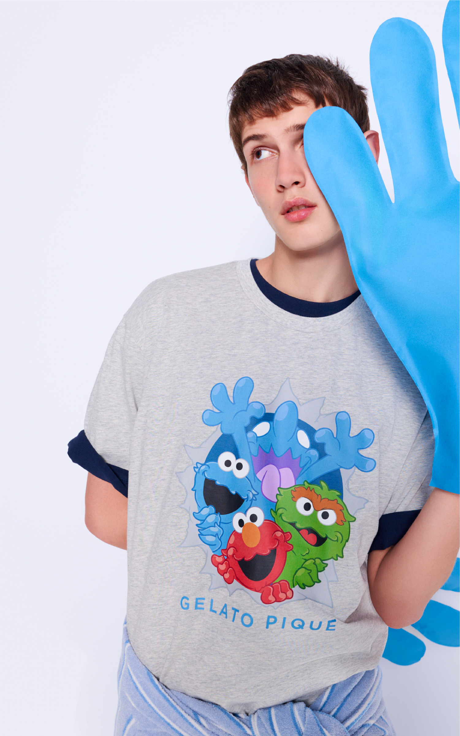 青い手袋を目もとにあてたモデル。セサミキャラクター柄のグレーTシャツを着用