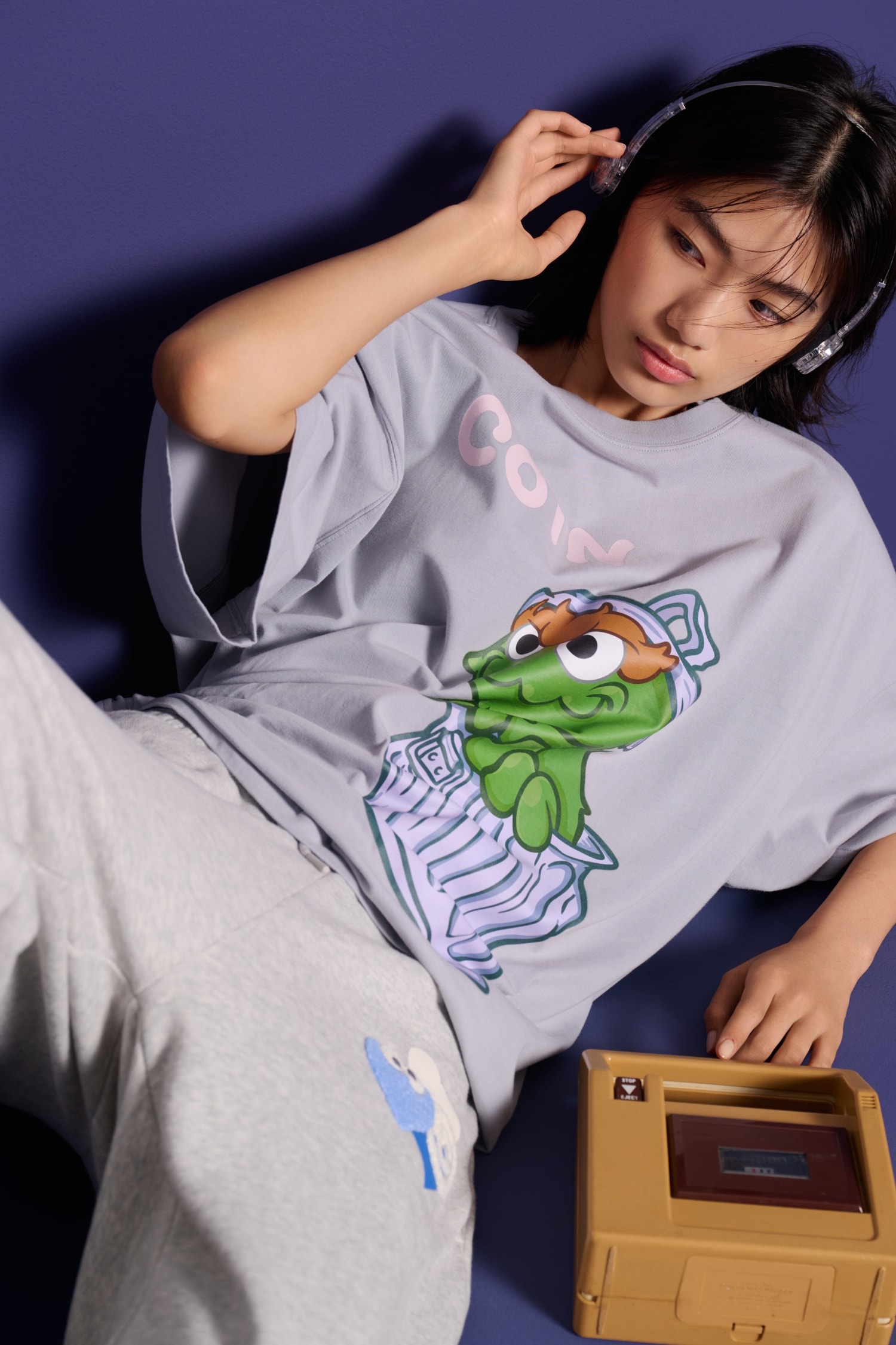 オスカー柄のグレーTシャツを着てくつろぐ女性モデル